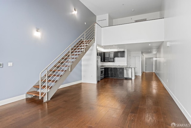 unfurnished living room with dark wood-type flooring and a towering ceiling