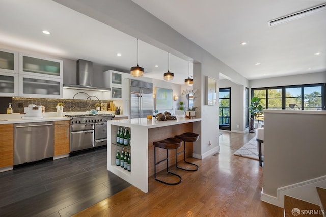 kitchen featuring a kitchen breakfast bar, dark hardwood / wood-style flooring, pendant lighting, high quality appliances, and wall chimney range hood