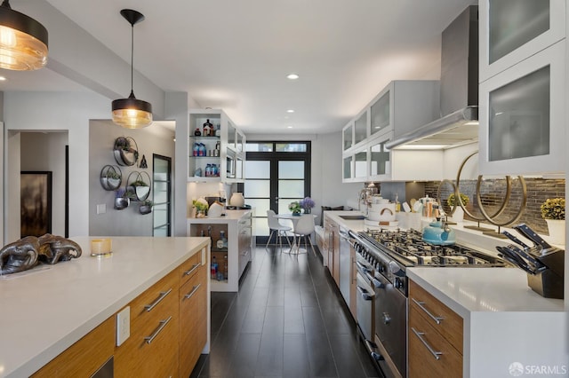 kitchen featuring stainless steel stove, wall chimney range hood, backsplash, decorative light fixtures, and dark hardwood / wood-style flooring