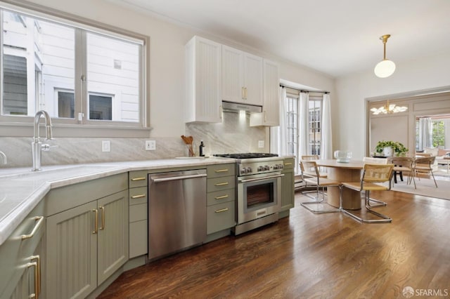 kitchen featuring appliances with stainless steel finishes, decorative light fixtures, light countertops, under cabinet range hood, and a sink