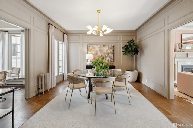 dining space with a chandelier, a decorative wall, a premium fireplace, ornamental molding, and radiator heating unit