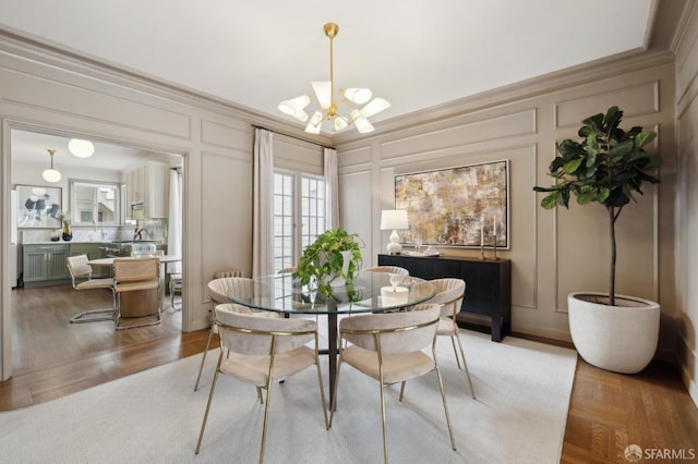 dining space featuring a notable chandelier, crown molding, wood finished floors, and a decorative wall