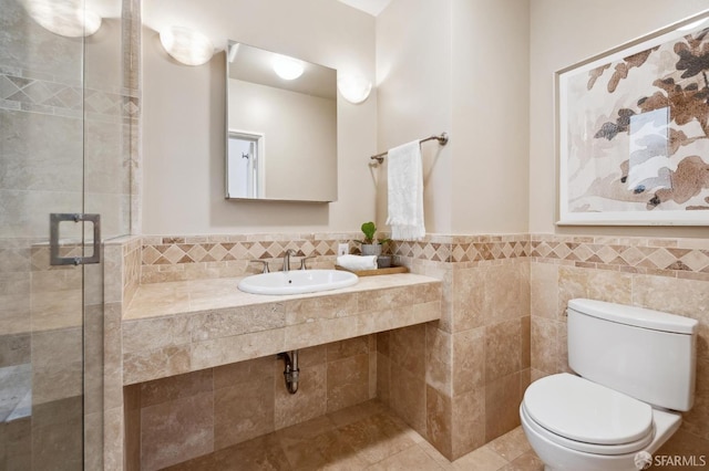 bathroom featuring toilet, a sink, tile walls, wainscoting, and a shower stall