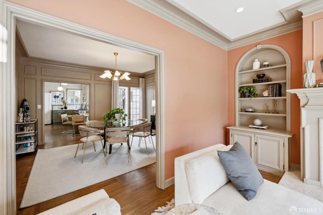 interior space featuring baseboards, ornamental molding, an inviting chandelier, light wood-type flooring, and built in shelves