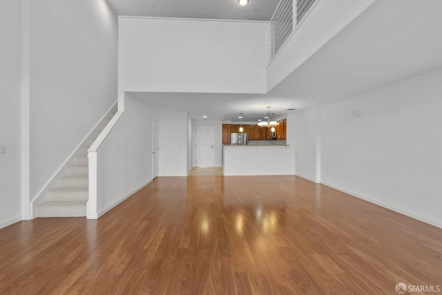 unfurnished living room featuring hardwood / wood-style floors, a notable chandelier, and a high ceiling