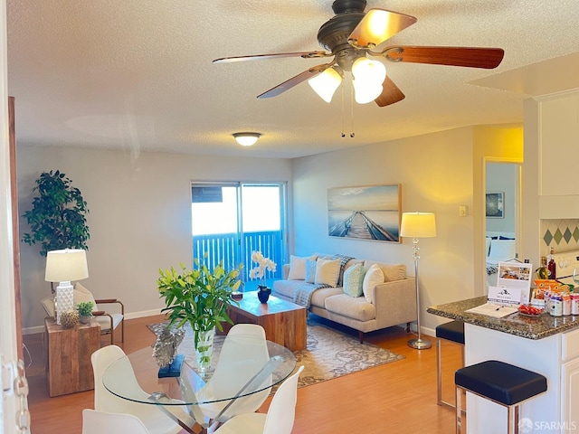 living room with ceiling fan, a textured ceiling, and light wood-type flooring