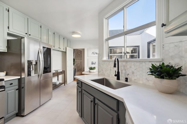 kitchen with gray cabinets, stainless steel fridge, tasteful backsplash, and sink