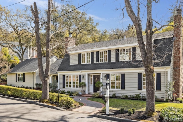 view of front of property featuring a chimney, a front yard, and a shingled roof