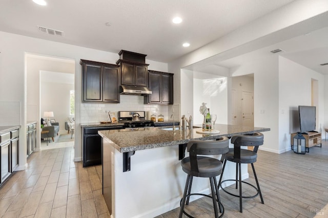 kitchen with a sink, stainless steel gas stove, tasteful backsplash, under cabinet range hood, and visible vents