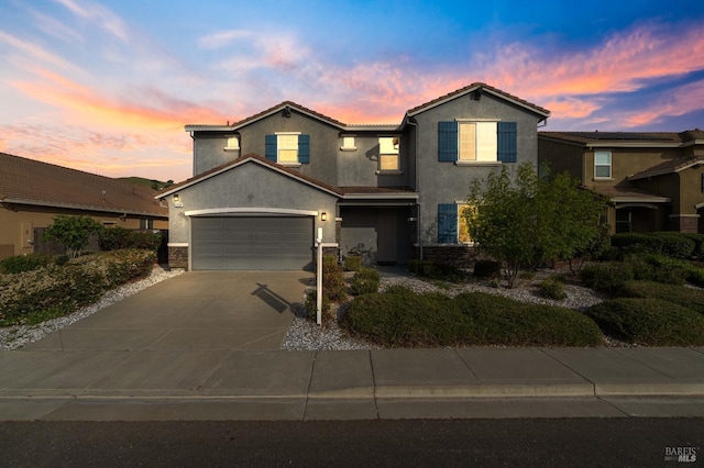traditional-style home with a garage, driveway, stone siding, and stucco siding
