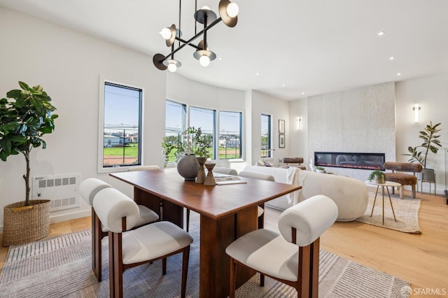 dining area with radiator heating unit, a fireplace, a chandelier, and light hardwood / wood-style floors