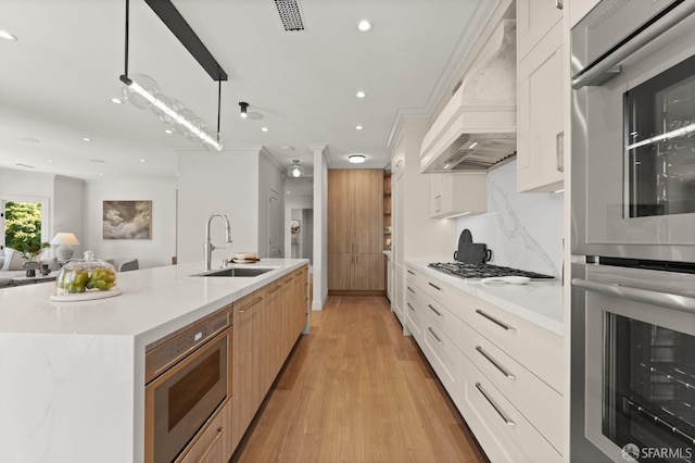 kitchen featuring white cabinets, pendant lighting, stainless steel appliances, light wood-type flooring, and sink