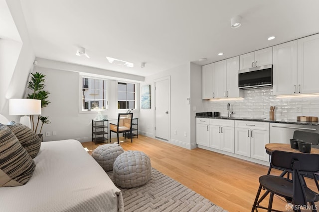 kitchen with light hardwood / wood-style flooring, appliances with stainless steel finishes, decorative backsplash, and white cabinetry