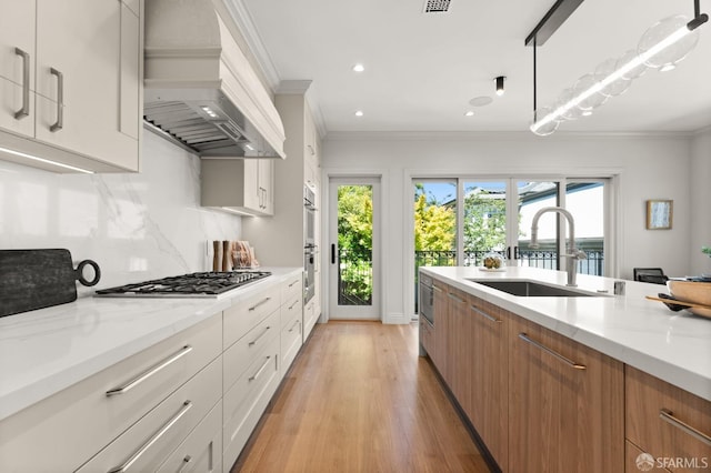 kitchen featuring light hardwood / wood-style floors, white cabinetry, custom exhaust hood, decorative light fixtures, and sink