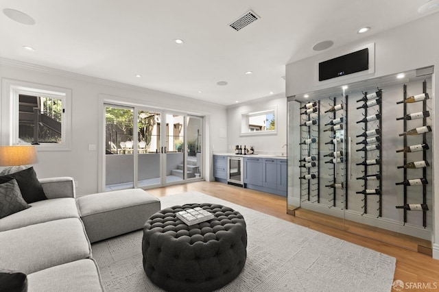 interior space with beverage cooler, light hardwood / wood-style flooring, bar, and ornamental molding