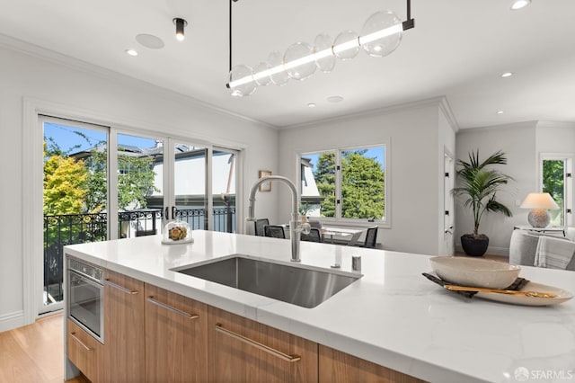 kitchen featuring light stone counters, light hardwood / wood-style floors, sink, hanging light fixtures, and crown molding