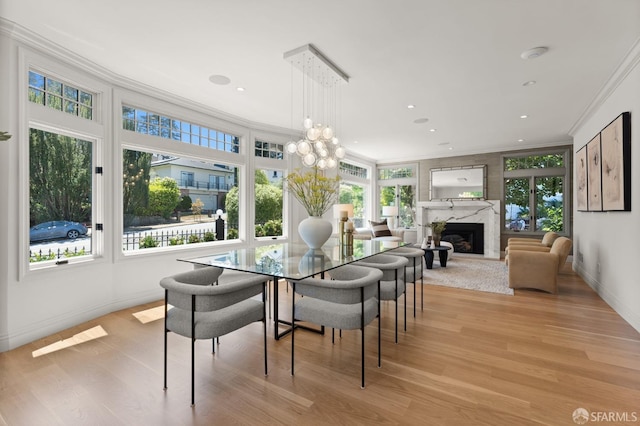 dining space with light wood-type flooring, a premium fireplace, ornamental molding, and a healthy amount of sunlight