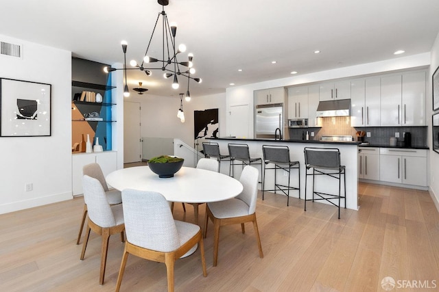 dining space with an inviting chandelier, light wood-type flooring, and sink