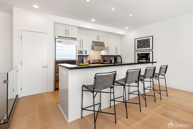 kitchen featuring a breakfast bar, white cabinets, kitchen peninsula, light hardwood / wood-style flooring, and built in fridge