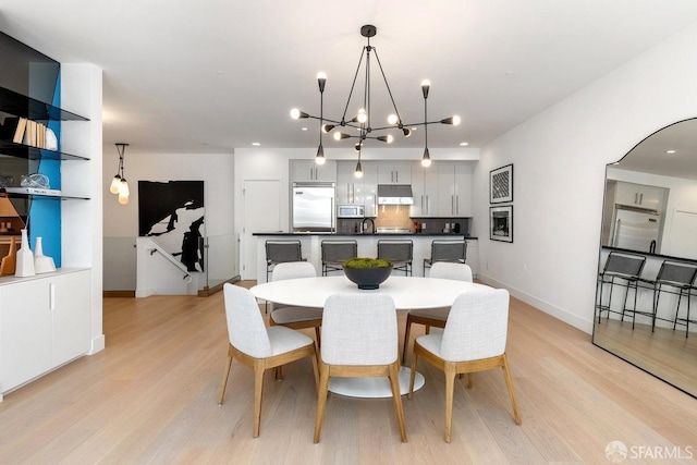 dining area with light wood-type flooring, sink, and a chandelier