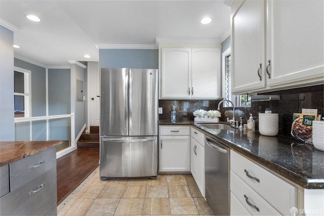 kitchen with sink, crown molding, white cabinetry, dark stone countertops, and stainless steel appliances