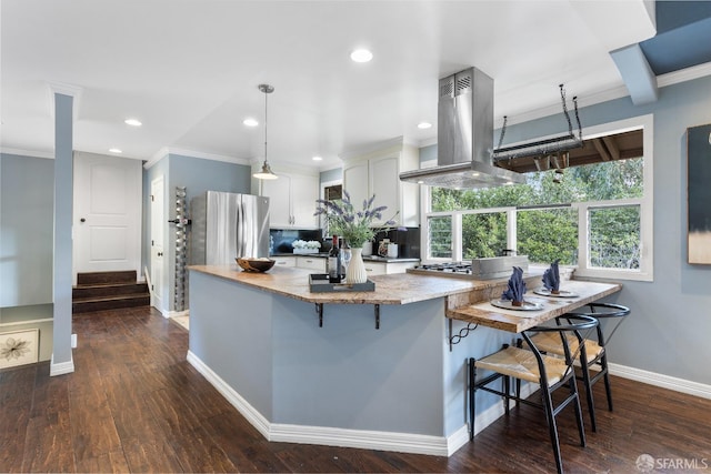 kitchen featuring appliances with stainless steel finishes, white cabinetry, island range hood, a kitchen bar, and decorative light fixtures