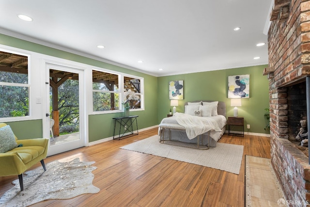 bedroom featuring crown molding, a brick fireplace, access to exterior, and light hardwood / wood-style flooring