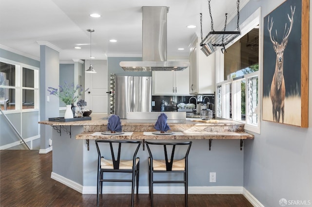 kitchen featuring a kitchen bar, stainless steel refrigerator, pendant lighting, island exhaust hood, and white cabinets