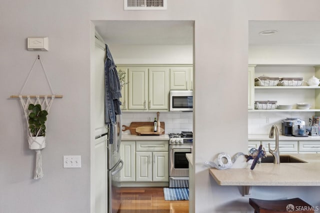 kitchen featuring sink, a breakfast bar area, appliances with stainless steel finishes, hardwood / wood-style flooring, and backsplash