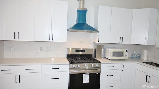 kitchen featuring tasteful backsplash, stainless steel gas range oven, light countertops, white microwave, and wall chimney exhaust hood