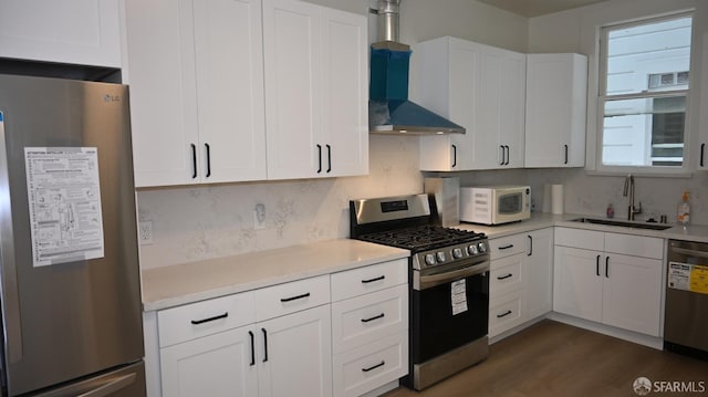 kitchen with light countertops, wall chimney exhaust hood, white cabinetry, a sink, and stainless steel appliances
