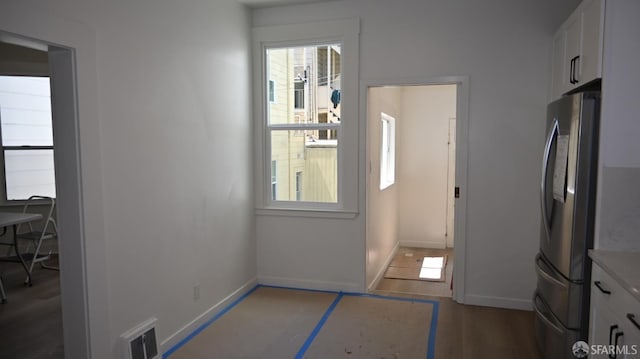 interior space featuring visible vents, freestanding refrigerator, baseboards, and white cabinetry