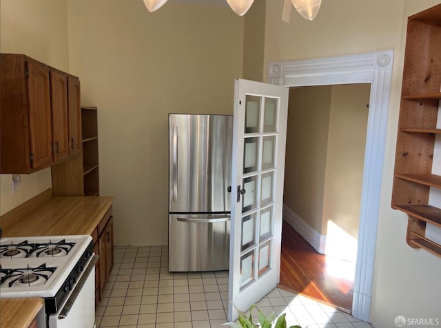 kitchen featuring white gas range, stainless steel fridge, and light tile patterned flooring