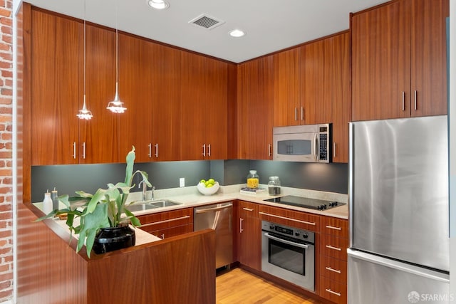 kitchen with sink, kitchen peninsula, decorative light fixtures, stainless steel appliances, and light hardwood / wood-style floors