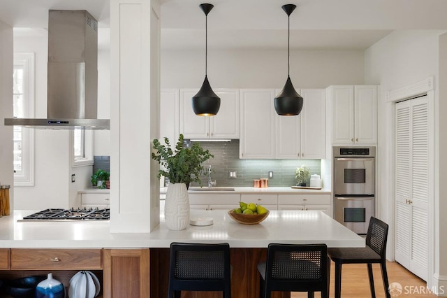 2864 Sacramento St, San Francisco, CA 94115 - kitchen featuring wall chimney exhaust hood, appliances with stainless steel finishes, a breakfast bar, white cabinetry, and decorative backsplash