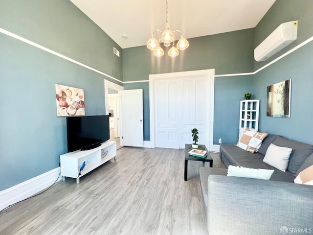 living room featuring a towering ceiling, a wall unit AC, an inviting chandelier, and light wood-type flooring