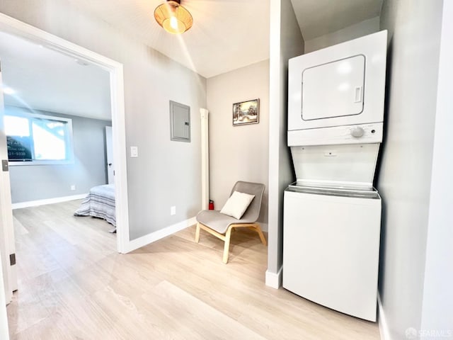 laundry area featuring electric panel, stacked washer and dryer, and light hardwood / wood-style floors