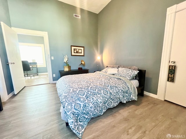 bedroom featuring a towering ceiling and light hardwood / wood-style floors