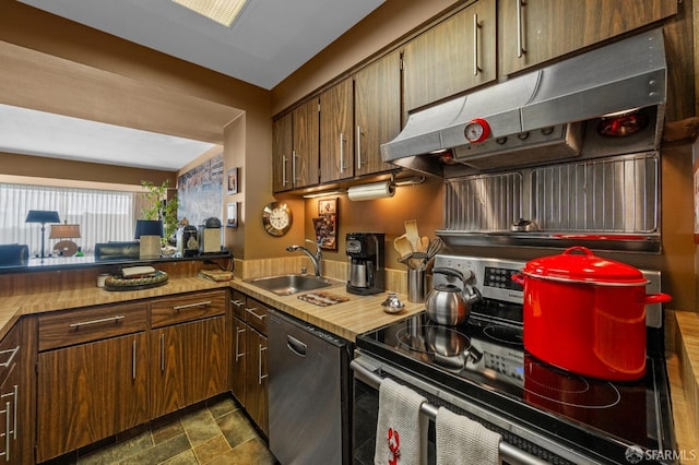 kitchen featuring under cabinet range hood, stone finish floor, stainless steel appliances, and a sink