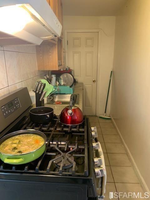 1326 Palou Ave, San Francisco, CA 94124 - kitchen featuring under cabinet range hood, stainless steel gas range, tile patterned flooring, baseboards, and decorative backsplash