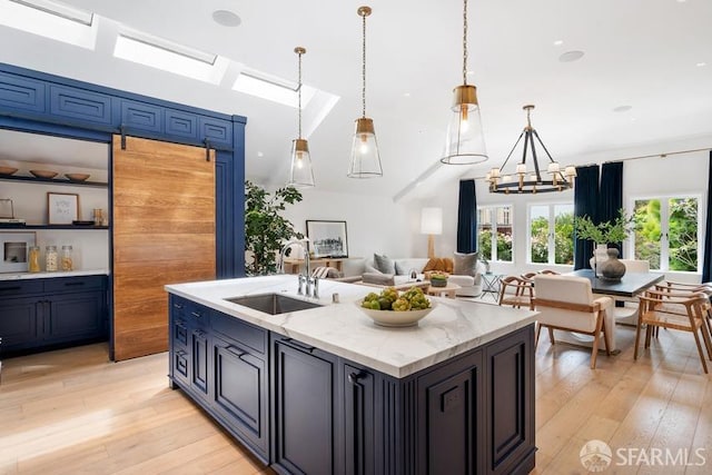 kitchen featuring a notable chandelier, light wood-style flooring, a sink, open floor plan, and light stone countertops