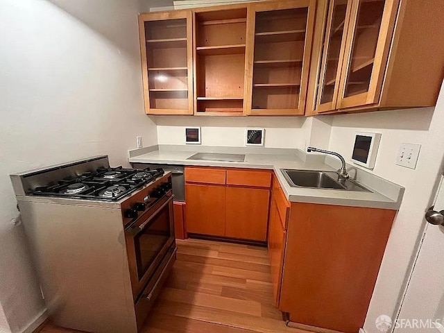 kitchen featuring stainless steel gas range oven, a sink, light countertops, light wood finished floors, and glass insert cabinets