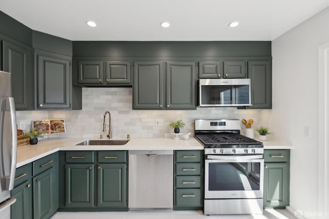 kitchen with a sink, light countertops, decorative backsplash, appliances with stainless steel finishes, and green cabinetry