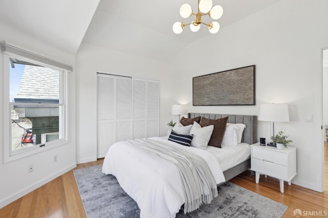 bedroom with vaulted ceiling, a notable chandelier, wood finished floors, and a closet