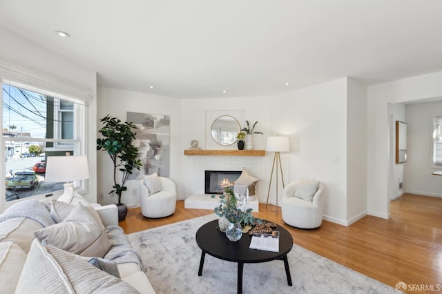 living area featuring a glass covered fireplace, baseboards, wood finished floors, and recessed lighting