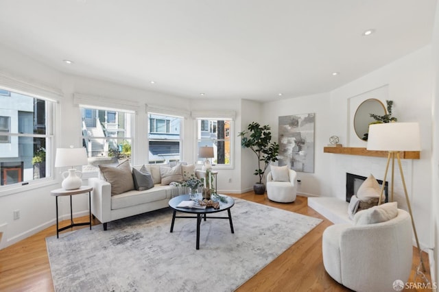 living area featuring recessed lighting, baseboards, light wood-style floors, and a fireplace with raised hearth