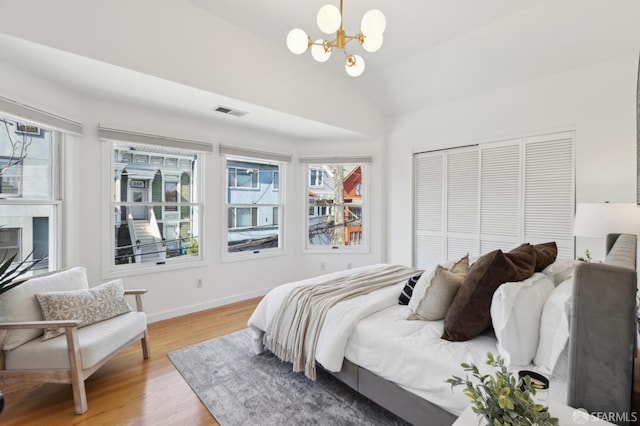 bedroom featuring visible vents, an inviting chandelier, lofted ceiling, a closet, and light wood-type flooring