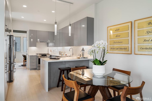 kitchen featuring a breakfast bar, gray cabinetry, hanging light fixtures, kitchen peninsula, and stainless steel appliances