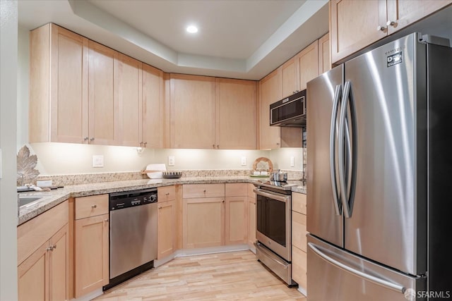 kitchen featuring light brown cabinets, light stone counters, stainless steel appliances, and light hardwood / wood-style flooring