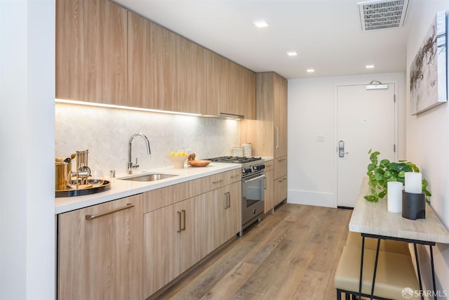 kitchen featuring sink, backsplash, high end stainless steel range oven, and light brown cabinets